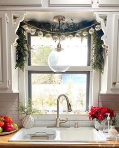 a kitchen sink under a window with christmas decorations on the windowsill and garland hanging over it