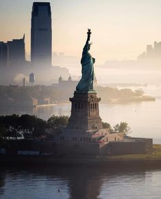 the statue of liberty in new york city on a foggy day with skyscrapers in the background