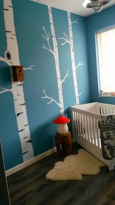 a baby's room decorated in blue and white with trees painted on the wall