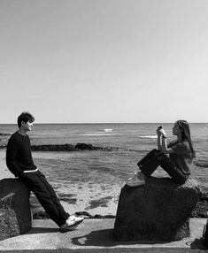 two people are sitting on rocks near the ocean and one is holding a cell phone