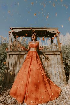 a woman wearing an orange dress standing in front of a wooden structure with leaves on it