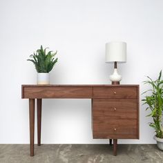 a wooden desk with two potted plants on it and a lamp next to it