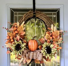 a fall wreath with pumpkins and flowers on the front door window sill,