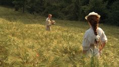 two people in a grassy field with trees in the background and one person wearing a straw hat