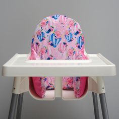 a high chair with a pink and blue seat cover on it's back, in front of a gray wall