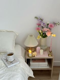 a nightstand with flowers and candles on it next to a bed