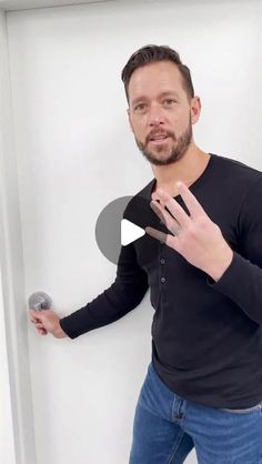 a man standing in front of a white wall with his hand on the door handle