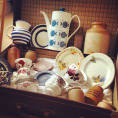 an open suitcase filled with dishes and tea cups on top of a table next to vases