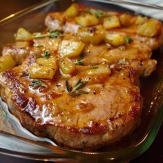 two pieces of meat with potatoes and herbs on it in a glass dish, ready to be eaten