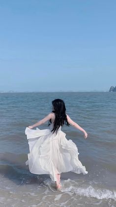 a woman in a white dress walking into the ocean