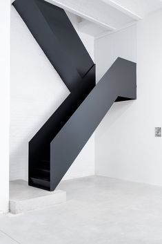 an abstract black sculpture in the middle of a white room with stairs leading up to it