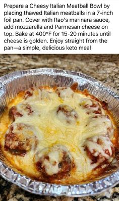 a pizza with meatballs and cheese on top in a tin foil pan sitting on a granite countertop