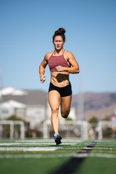 a woman running on a field with grass and buildings in the background