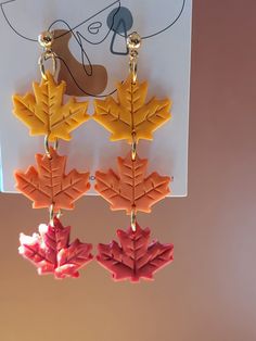 three leaf shaped earrings hanging from hooks in front of a white board with a drawing on it