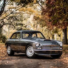 an old car is parked on the side of the road in front of some trees