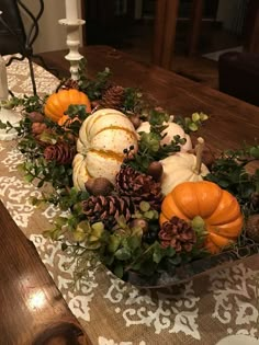 a basket filled with pumpkins and pine cones on top of a table covered in greenery