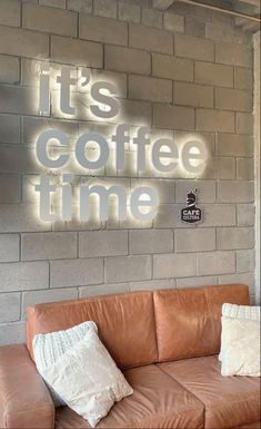 it's coffee time neon sign on the wall above a leather couch with pillows