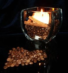 coffee beans, cinnamon sticks and lit candle in glass container on black table with dark background