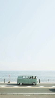 an old vw bus is driving down the road by the ocean in front of it