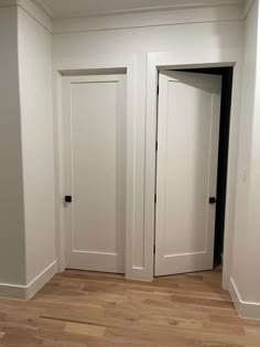 an empty room with two white doors and hard wood floors