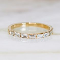 a gold wedding band with baguettes and diamonds on the side, sitting on a marble surface