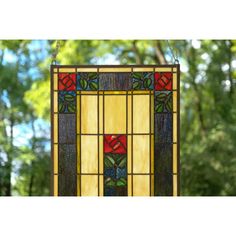 a stained glass window hanging from the ceiling in front of some trees and bushes with green leaves on it