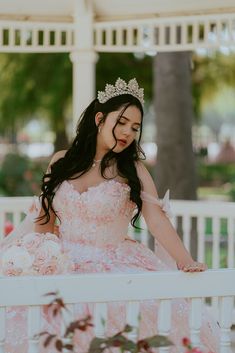 a woman in a pink dress sitting on a bench wearing a tiara and holding flowers