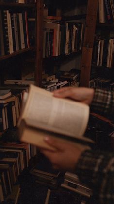 a person is holding an open book in front of bookshelves