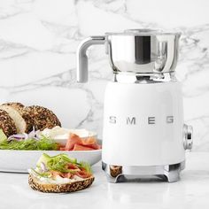 a white blender sitting on top of a counter next to a plate of food