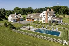 an aerial view of a large house with a pool in the foreground and several lawn chairs around it