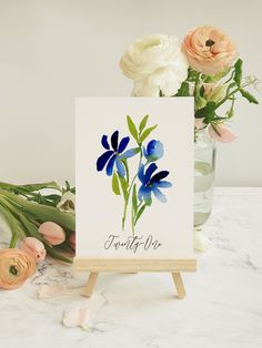 a card with blue flowers on it sitting next to a vase filled with pink and white flowers