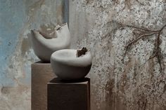 two white vases sitting on top of each other in front of a concrete wall