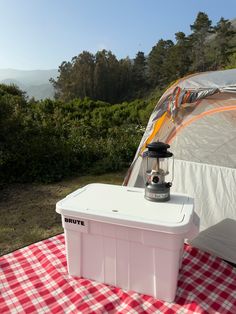 a cooler sitting on top of a red and white checkered tablecloth next to a tent