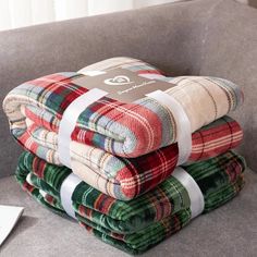 four plaid blankets stacked on top of each other in front of a gray couch with white ribbon