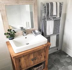 a white sink sitting under a bathroom mirror next to a wooden cabinet and towel rack