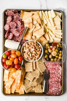 an assortment of cheeses, crackers, meats and vegetables on a tray