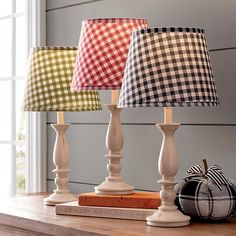 three lamps sitting on top of a wooden table next to a book and pumpkins