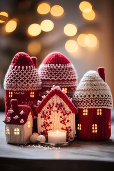 small knitted houses with lit candles in front of them on a table next to christmas lights