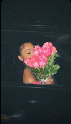 a woman is holding pink roses in the back of a truck at night, with her eyes closed