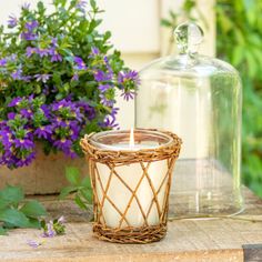 a wicker candle holder sitting on a table next to purple flowers and a glass jar