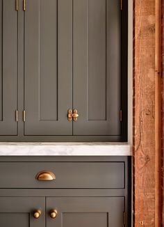 a kitchen with gray cabinets and white counter tops, gold pulls on the handles in front of it