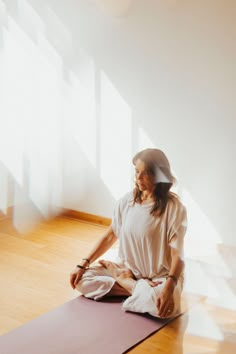 a woman sitting on top of a yoga mat in the middle of a room with sunlight streaming through the window