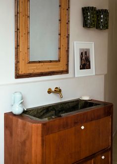 a bathroom sink sitting under a mirror next to a wall mounted faucet in front of a wooden cabinet