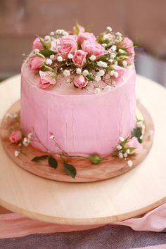 a pink frosted cake with flowers on top sitting on a wooden platter, ready to be eaten