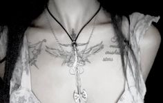 a woman with tattoos on her chest wearing a cross and angel pendant necklace in black and white