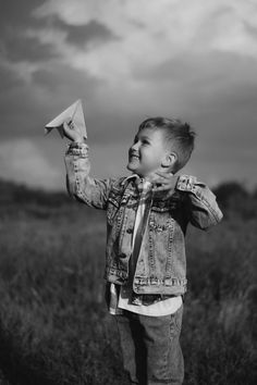 a little boy that is standing in the grass holding a paper airplane up to his face