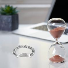 an hourglass sitting on top of a table next to a laptop and a bracelet