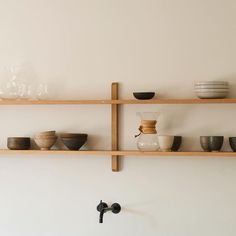 shelves with bowls and cups on them against a white wall behind a faucet