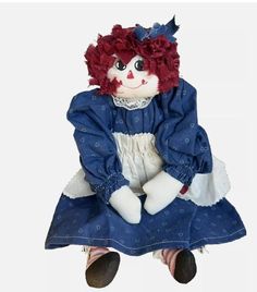 a ragged doll sitting on the ground wearing a blue dress