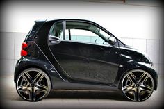 a smart car parked in front of a white wall with black rims and chrome spokes